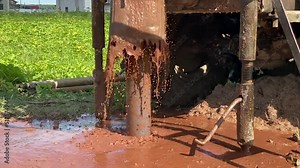Aquifer Detection. A stream of dirty water springs from a gushing well against the background of a drilling mechanism