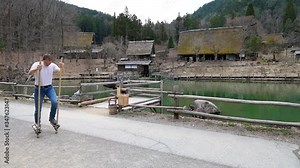 Slow motion of man tourist having fun walking on stilts wooden traditional Japanese sticks in Hida no Sato folk village, Takayama, Gifu prefecture of Japan