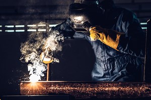 Tukang las logam bekerja dengan mesin pengelasan busur.