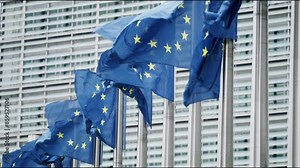 In Brussels, the political heart of the European Union, several EU flags flutter in harmony beside a contemporary glass building, embodying unity and progressiveness in a symbolism rich scene