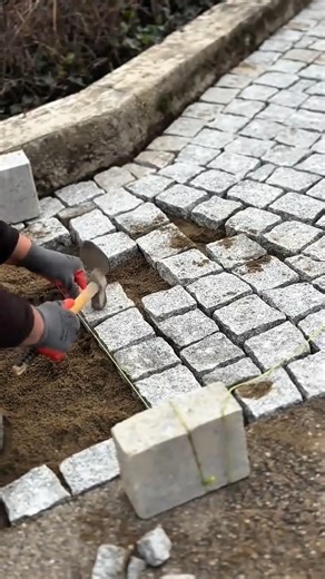 laying natural stone paving blocks on a sand base using a hammer tool for a garden path project