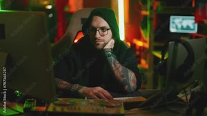 Hacker writing code cracking computer. Man programmer in hoodie cracks system, using computer in dark room. Hacker attack, technology, virus infected software, dark web, cyber security concept.