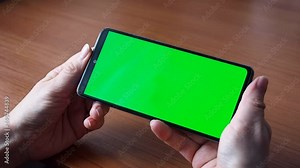 The green screen of a smartphone or chroma key. Women's hands hold the phone, click the touch screen. Close up Mock up