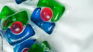 Laundry capsules falling on fabric from top to bottom, vertical slow motion.