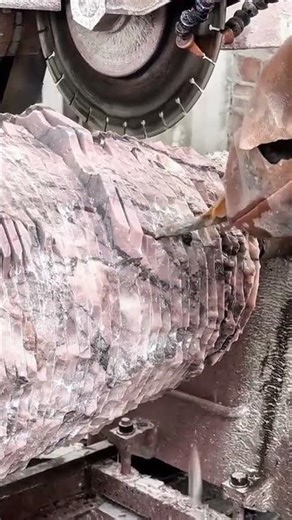 Cutting a large piece of raw pink stone using a heavy industrial saw machine