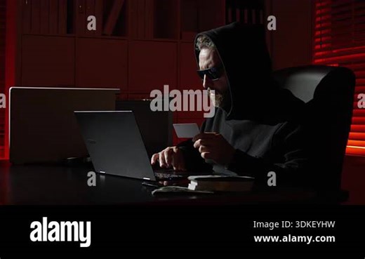hacker typing code in dark office. Masked hacker hacking a computer in night room. Night hacker attack network security. Cyber hacker and data security. Digital credit card fraud