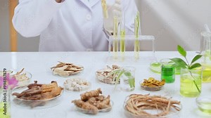 Scene on white lab bench with several types of herbal ingredients contained in lab glassware, scientist sitting by the table and conducting an experiment. High angle shot, editing space