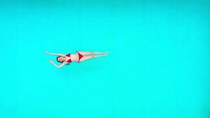 View from the top as a woman in red swimsuit lying on her back in the pool. Relaxing concept