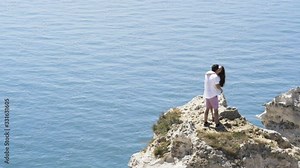 Couple in love by the sea kissing and standing above blue rippled water. Action. Boy and girl at the sea traveling during honeymoon, holiday romance.