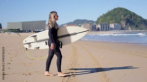 Female surfer walking on the beach to the water.