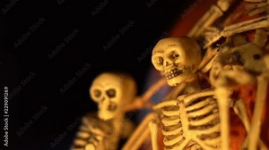Small plastic skeletons draped over a Halloween pumpkin. Closeup, low light. Stock Video