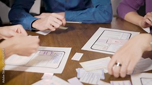 Brainstorm. In the frame are the hands of designers and layouts of the mobile application. Developers work on functionality at the design stage.