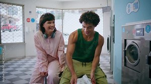 Two happy friends laughing in public laundromat. Carefree teenagers washing
