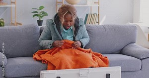 Afro American female at home, frozen in freezing cooled flat in warm coat, blanket shivering tremble with cold, unhappy lady feels bad suffer of heating system problem, climate, temperature regulation