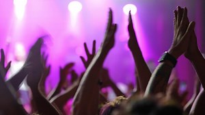 Crowd of enthusiastic concertgoers with hands raised, enjoying live music under colorful stage lights, creating an energetic atmosphere