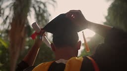 A man wearing a black and yellow graduation cap and gown is holding a...