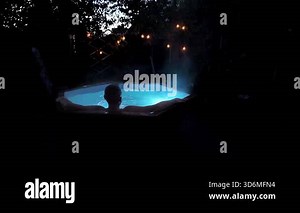 Person relaxing in steaming outdoor hot tub at night. High quality FullHD footage