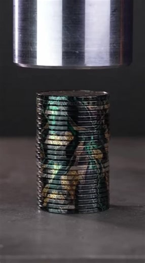 Nic Davis on Instagram: "Watch as a towering stack of black marble-coated nickels gets obliterated under a hydraulic press. The coins bow and compress, releasing a mesmerizing graphite-gray pearlescent paste that oozes out in the most satisfying way possible."