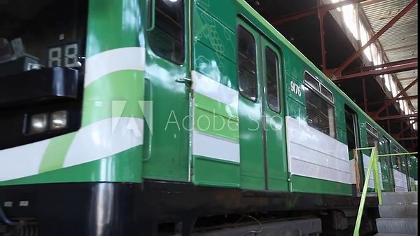 Green subway train moves in a maintenance depot followed by a traffic light changing from green to red signal on a city street and parked blue metro cars.