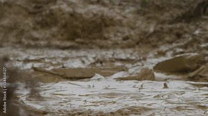 Slow motion close up mud splash in mud puddle surrounded by dirt