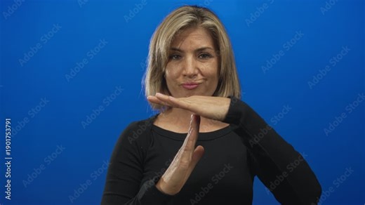 Woman holds hands up forming time out gesture in studio against blue backdrop with serious expression; caution.