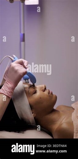 Professional beautician in pink gloves using blue microcurrent devices on an African American womans face. Modern lifting and skincare treatment Stock Video Footage - Alamy