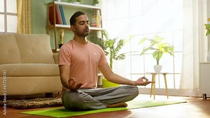 Peaceful indian man doing meditation on yoga mat with eyes closed during morning at home - concept of tranquility, Mindfulness and self care.