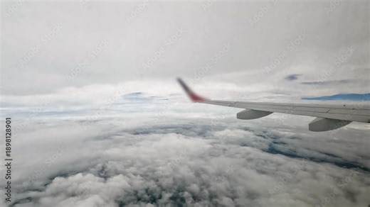 Port side wing of commercial jet airliner flying through cloud sky