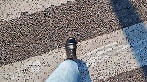 Women's legs walk down the street, first person view. A pedestrian's legs walk across a road zebra crossing. Close-up of human legs, walking outdoors. Spring, autumn or winter, comfortable shoes