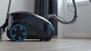 A vacuum cleaner with a wet cleaning function is in the room. Black with blue elements vacuum cleaner on a light oak floor on a background of light walls and dark gray curtains