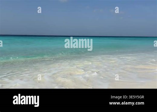A wide shot of a serene tropical coastline featuring crystal-clear turquoise water and gentle white waves crashing on a pristine sandy beach under a clear blue sky during a bright sunny day. Cas Abao Beach, Curacao. High quality 4k footage Stock Video Footage - Alamy