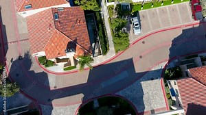 overhead tilt aerial footage of pools and lush green palm trees with the blue waters of Huntington Harbour and homes with blue sky, clouds and cars driving on the street in Huntington Beach California