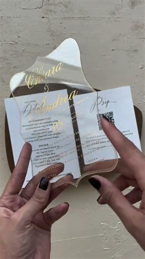 This acrylic wedding invitation features a rich wood-toned backdrop, delicate gold foil script, and