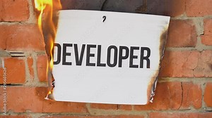 The inscription on a white A4 size sheet against the background of an orange brick wall. The paper with the black word Developer burns, smoke and turns into ashes. Business concept.