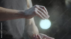 Professional male athlete clapping hands and applying chalk powder to palms while getting ready for gym workout. Close-up view, slow mo