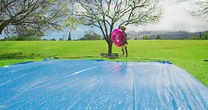 Summer water slide fun, smiling young boy sliding down waterslide on innertube