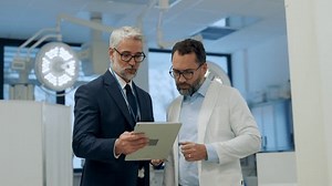 Pharmaceutical sales representative presenting new medication to doctor in medical building, holding box with medication samples.