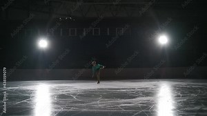 Slow motion: Cinematic shot of young female artistic figure skater is performing a woman's single skating choreography on ice rink before start of a competition. Concept of freedom