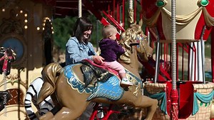 A mother and her baby daughter enjoy a fun day out riding a carousel together at an amusement park.