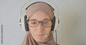 Face of woman in hijab, muslim female talking in headphones with microphone, close-up, portrait. Concept of remote learning, work, call center, customer support.