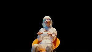 A young futuristic woman with an electronic device on her hands sits on a yellow char and starts typing into the air - Free Stock Video