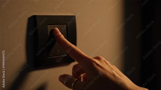 Finger pressing modern black smart switch on wall to turn on indoor light.