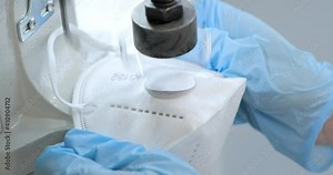 A worker in a protective suit connects a medical FFP3 mask. Hands insert the filter valve into the protective mask. Production of clothing for protection against the virus. Medicine clothing factory.