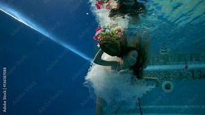 girl in short, white dresses wearing poses underwater in swimming pool