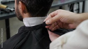 Barber putting a cape on his customer for a haircut in a barbershop.