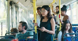 Bus stands at downtown bus stop woman with glasses taking public transportation clings to railing, looks at phone writes back to friends, browses social media occupie time during the long ride home