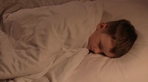 small child boy tosses restlessly in sleep on a pillow under a blanket at night. Sleeping preschooler kid son on bed in bedroom in the evening