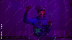 Girl Using Virtual Reality Headset And Looking Around At Interactive Technology With Colorful Illumination. VR Entertainment Immersive. Girl Wearing VR Headset in World of Virtual Reality Interacting.
