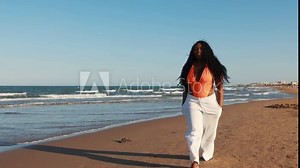 Beautiful African American woman in orange bikini on tropical beach. Portrait of dark-skinned woman smiling in sea. Brunette tanned girl in swimsuit enjoying and walking on beach.
