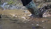 Unrecognizable woman steps in rubber boots into a muddy puddle, slow...